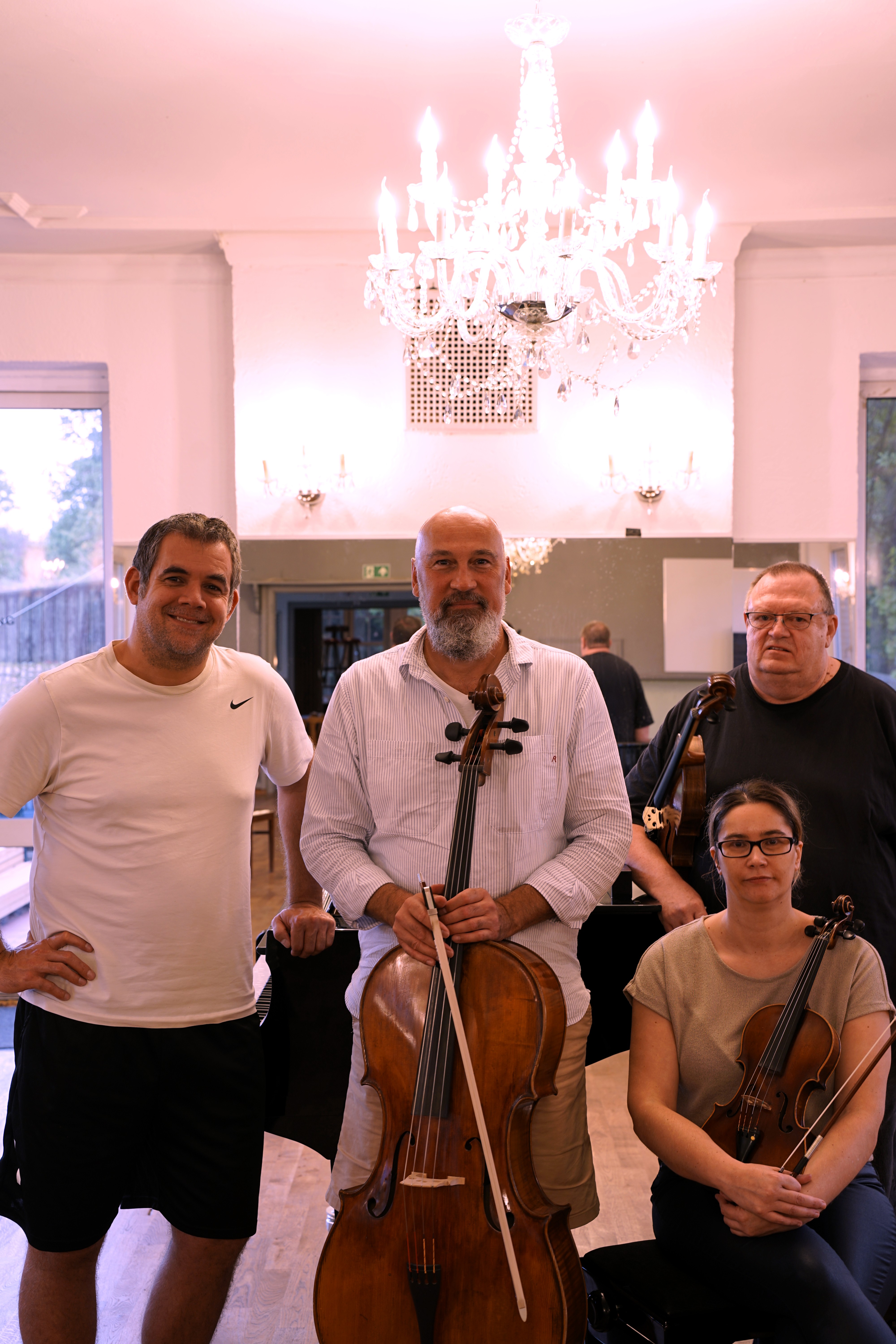 Vier Mitglieder eines Streicherensembles posieren mit Cello und Violinen in einem hellen Saal unter einem großen Kristallleuchter.